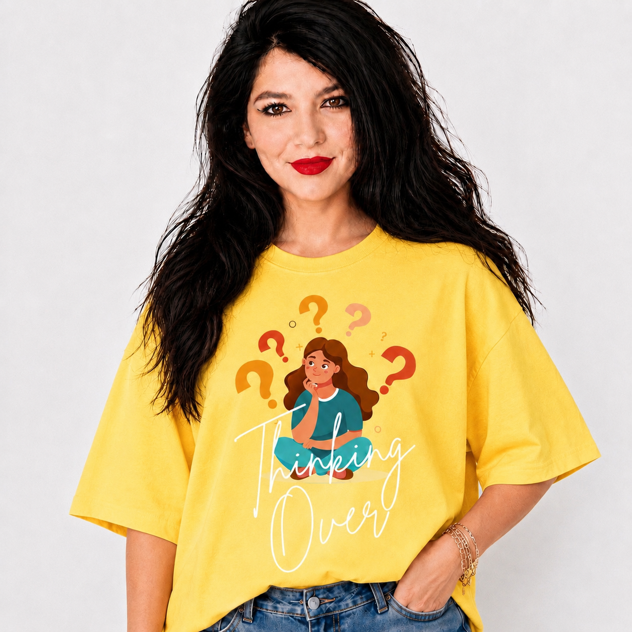 A woman with long black hair wearing a bright yellow graphic t-shirt that reads 'Thinking Over' with an illustration of a woman surrounded by question marks, paired with blue jeans against a light gray background.