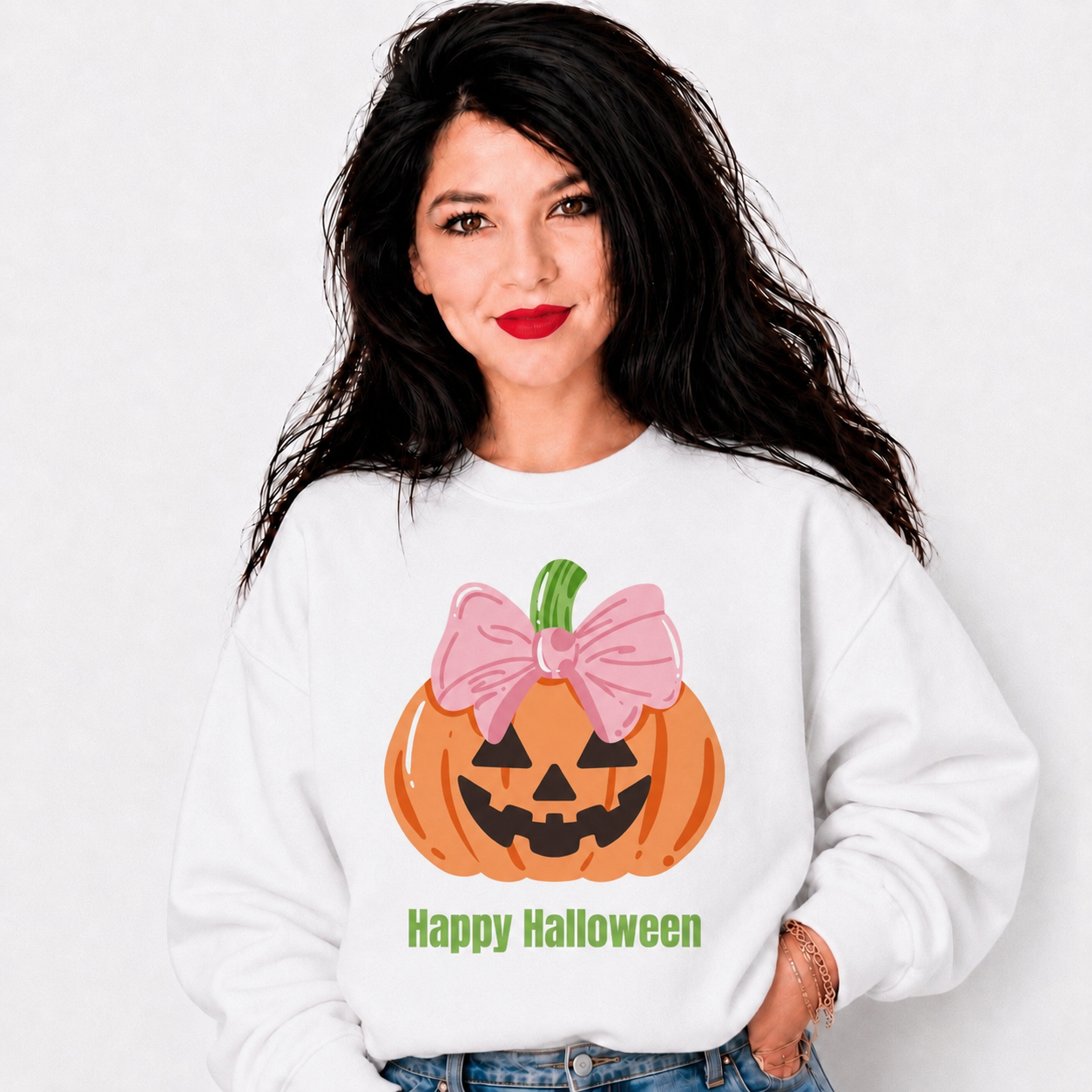 A woman wearing a white crewneck sweatshirt with a cartoon jack-o'-lantern graphic wearing a pink bow and the text 'Happy Halloween' printed below it.